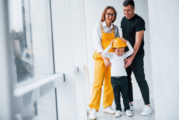 Female worker in yellow uniform standing indoors with man and child. - Photo, image