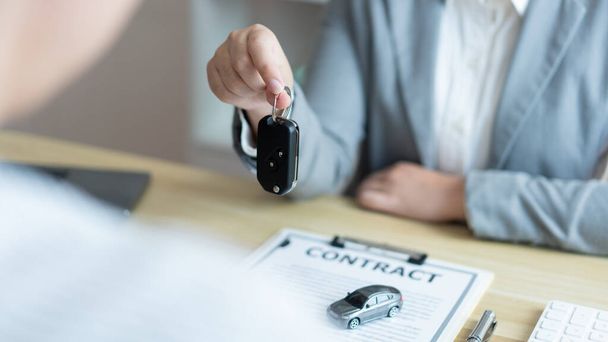 Ασφαλιστική έννοια ο έμπορος αυτοκινήτων εξηγώντας τους όρους του αυτοκινήτου, ενώ δείχνει ένα κλειδί αυτοκινήτου για τον πελάτη του. - Φωτογραφία, εικόνα