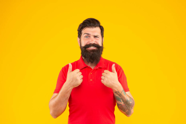 happy bearded man with moustache in tshirt showing thumb up on yellow background, mens beauty - Valokuva, kuva