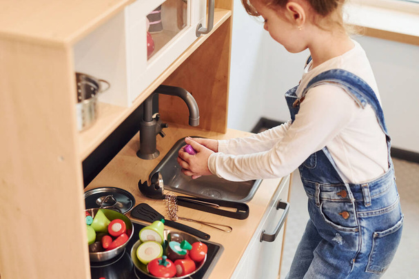 Little girl in casual clothes have fun by playing with toys on the kitchen. - Foto, imagen