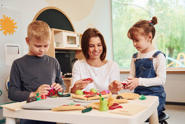 Young woman with little boy and girl playing with toys together on the kitchen. - 写真・画像