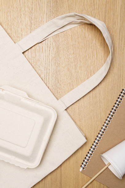 Οικολογικό concept, χάρτινο κύπελλο με καλαμάκια σημειωματάριο και κουτιά σε οικολογική τσάντα πάνω από ξύλινο φόντο. - Φωτογραφία, εικόνα