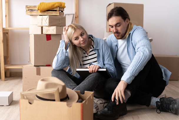 Пара переезда в дом, счастливая пара расслабляясь, сидя рядом картонные коробки в новом доме, люди, переезд и концепция недвижимости - Фото, изображение