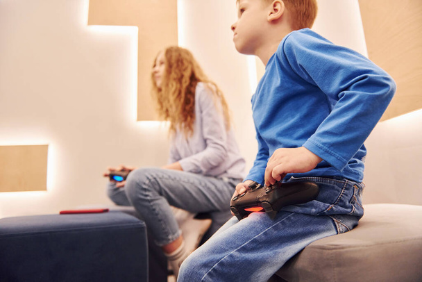 Cheerful kids sitting indoors and playing video games together. - Valokuva, kuva
