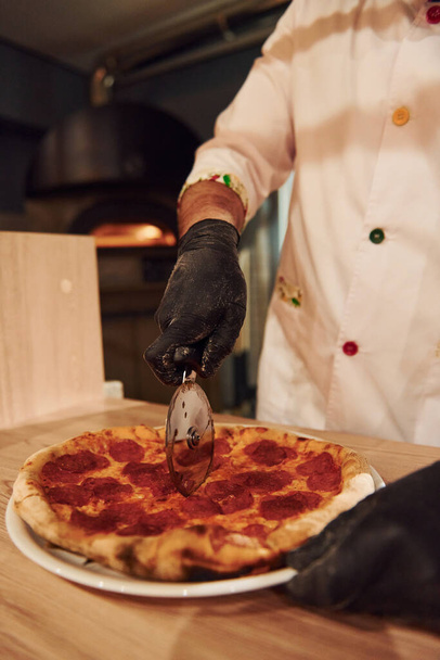 Kokki valkoisissa vaatteissa valmistelee herkullista pizzaa ravintolan keittiössä. - Valokuva, kuva