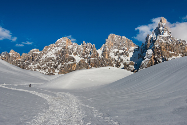 Een wandelaar op een pad in de titel van de sneeuw van Pale van San Martino bergketen in een dag met blauwe hemel met wolken, Dolomieten, Italië - Foto, afbeelding