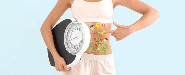 Young woman with floor scales and healthy vegetables on her body against blue background. Concept of diet - Foto, imagen