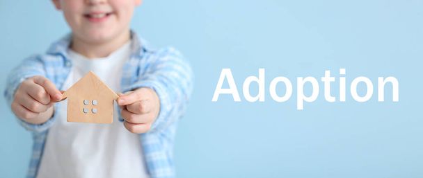 Cute little boy with figure of house on color background. Adoption concept - Photo, Image