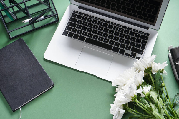 Ноутбук с канцелярскими принадлежностями и цветами на зеленом фоне - Фото, изображение