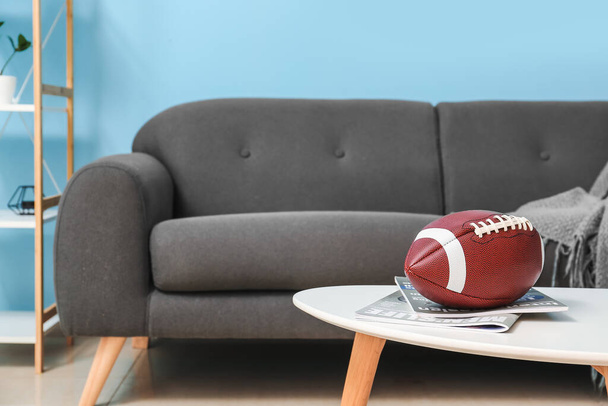 Pallone da rugby e riviste sul tavolo vicino al divano in soggiorno - Foto, immagini