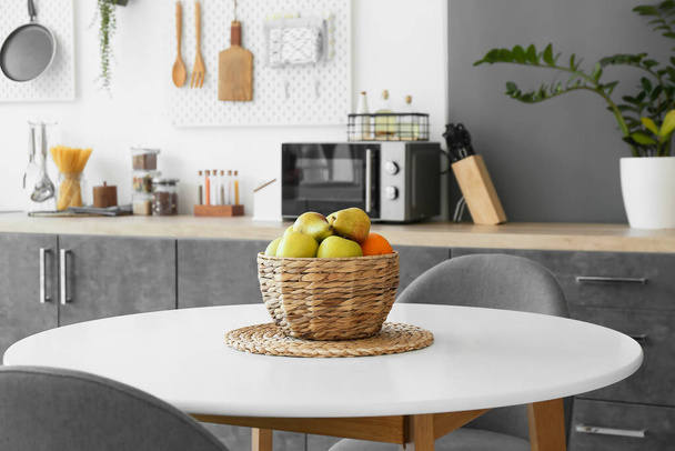 Wiklinowy kosz ze świeżymi owocami na stole w kuchni - Zdjęcie, obraz