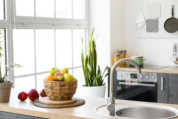 Wicker basket with delicious fruits on counter in modern kitchen - Φωτογραφία, εικόνα