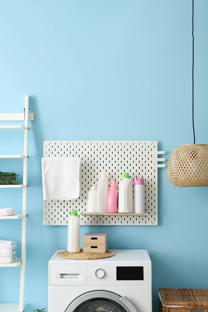 Pegboard com garrafas de detergente e máquina de lavar roupa moderna perto da parede de cor na lavanderia - Foto, Imagem