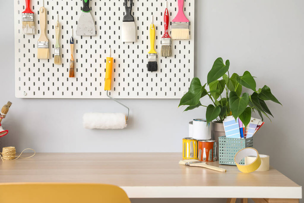 Desk with paint samples, houseplant and pegboard with tools on light wall - Foto, imagen