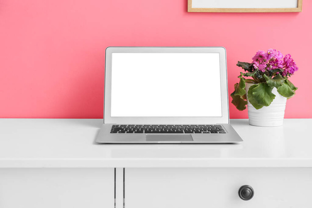Робоче місце з сучасним ноутбуком і квітучою рослиною біля кольорової стіни
 - Фото, зображення