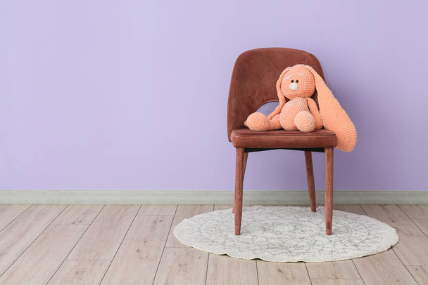 Chair with toy rabbit near violet wall in room - Foto, Imagen