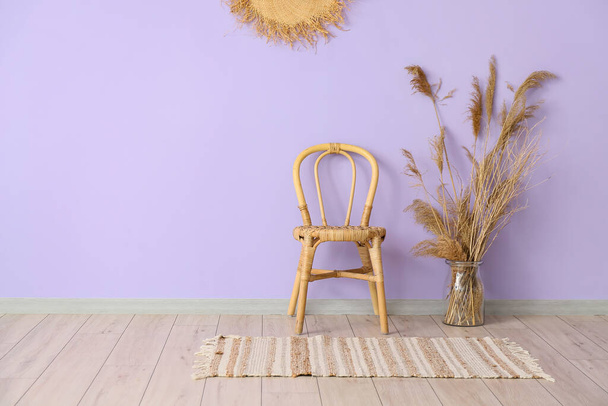 Плетеный стул и ваза с тростниковыми цветами возле фиолетовой стены в интерьере комнаты - Фото, изображение