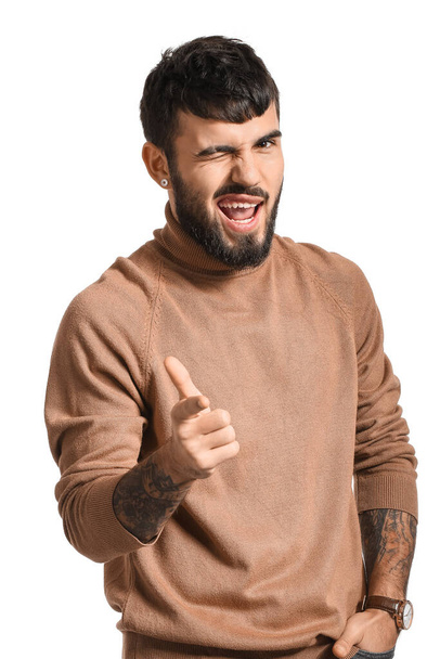 Young bearded man pointing at viewer and winking on white background - Foto, immagini