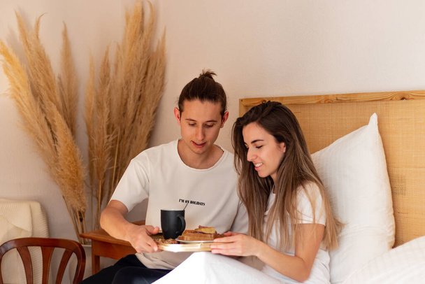 Apreciative young woman beacuse of her boyfriend surprised in bed. Happy couple having breakfast - Фото, зображення
