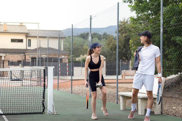 Mężczyzna i kobieta patrząc na siebie przybywających na kort tenisowy z rakietami podczas śmiechu i rozmowy - Zdjęcie, obraz