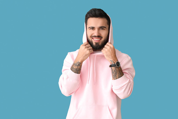 Young bearded man wearing stylish hoodie on blue background - 写真・画像