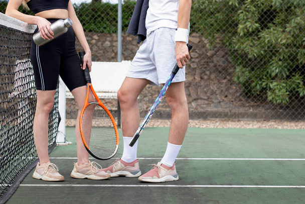 Side view of fit in shape young man and woman chatting after a tennis match relaxed closed to the net - 写真・画像