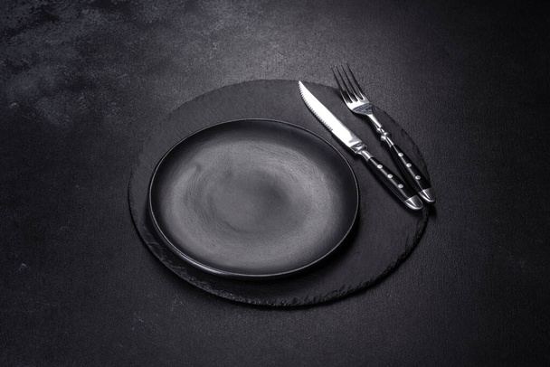 Platos negros vacíos, tenedor y cuchillo sobre un fondo negro. Vista superior, espacio de copia - Foto, Imagen