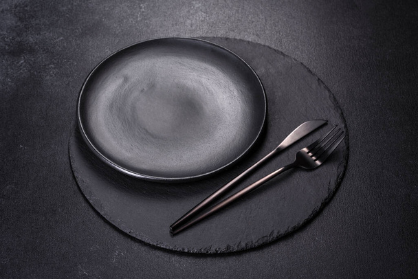 Üres fekete tányérok, villa és kés fekete háttérrel. Felülnézet, másolás - Fotó, kép