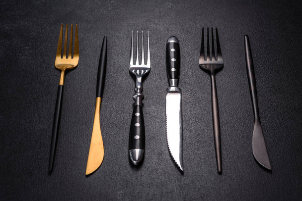 Kilka noży i widelców w czarnym złocie i srebrze na ciemnym betonowym tle. Przygotowanie stołu do obiadu - Zdjęcie, obraz