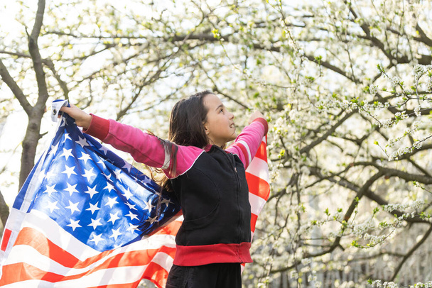 Χαρούμενο αξιολάτρευτο κοριτσάκι να χαμογελάει και να ανεμίζει αμερικάνικη σημαία. Πατριωτική γιορτή. Ευτυχισμένο παιδί, χαριτωμένο κοριτσάκι με αμερικανική σημαία. Οι ΗΠΑ γιορτάζουν την 4η Ιουλίου. Έννοια της ημέρας ανεξαρτησίας. - Φωτογραφία, εικόνα