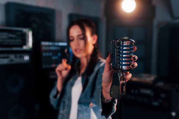 Close up view of microphone. Young beautiful female performer rehearsing in a recording studio. - Valokuva, kuva