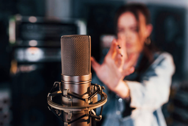 Close up view of microphone. Young beautiful female performer rehearsing in a recording studio. - Foto, Imagem