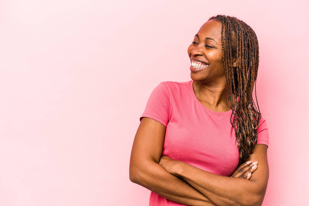 Junge afrikanisch-amerikanische Frau isoliert auf rosa Hintergrund lächelt selbstbewusst mit verschränkten Armen. - Foto, Bild