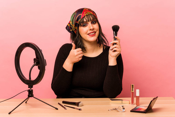 Young makeup artist woman doing a makeup tutorial isolated on pink background smiling and raising thumb up - Foto, immagini
