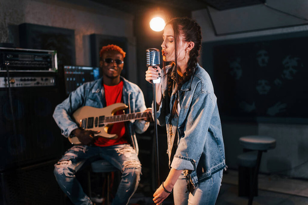 Guy plays guitar, girl sings. African american man with white girl rehearsing in the studio together. - Foto, Imagen