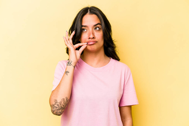 Young hispanic woman isolated on yellow background with fingers on lips keeping a secret. - Фото, изображение