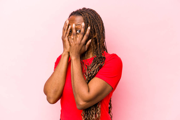 Young african american woman isolated on pink background blink through fingers frightened and nervous. - Фото, зображення