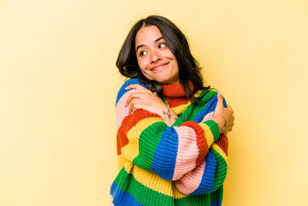 Junge hispanische Frau isoliert auf gelbem Hintergrund umarmt, lächelt unbeschwert und glücklich. - Foto, Bild