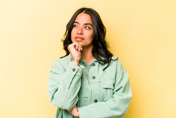Young hispanic woman isolated on yellow background thinking and looking up, being reflective, contemplating, having a fantasy. - Фото, изображение
