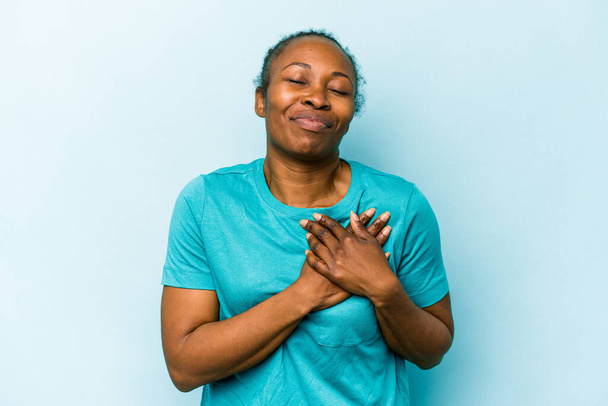 Νεαρή Αφροαμερικάνα που απομονώνεται σε μπλε φόντο έχει φιλική έκφραση, πιέζοντας την παλάμη στο στήθος. Έννοια αγάπης. - Φωτογραφία, εικόνα