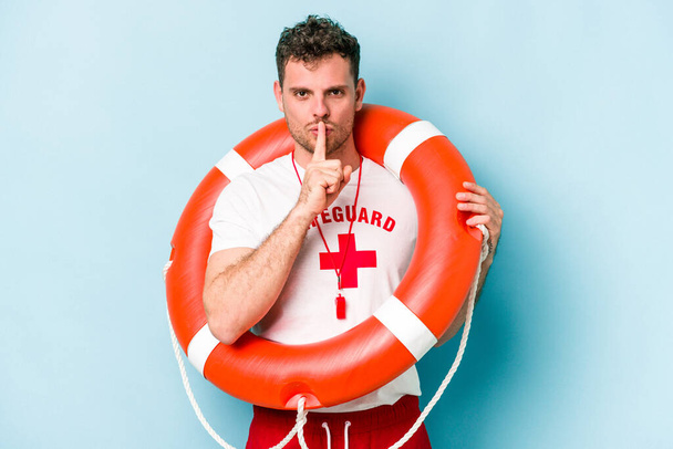 Young caucasian lifeguard man isolated on blue background keeping a secret or asking for silence. - Foto, Imagen
