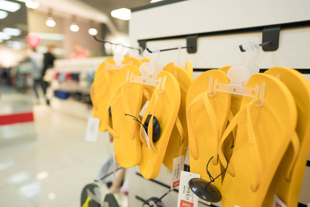 Żółte letnie wodoodporne obuwie plażowe w sklepie obuwniczym - nowa kolekcja mody w modnym sklepie. Koncepcja odsprzedaży. Stojak na buty na niewyraźne tło sklepu z przestrzenią do kopiowania - Zdjęcie, obraz