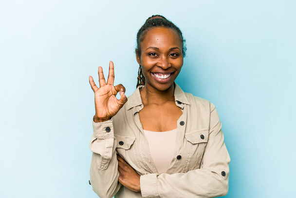 Nuori afrikkalainen amerikkalainen nainen eristetty sinisellä taustalla iskee silmää ja pitää kunnossa ele käsin
. - Valokuva, kuva