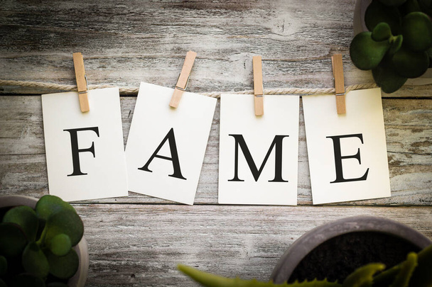 A set of printed cards spelling the word FAME on an aged wooden background. - Photo, Image
