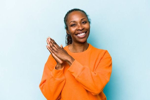 青の背景に隔離された若いアフリカ系アメリカ人の女性は、精力的で快適な感じ、手をこすり自信. - 写真・画像