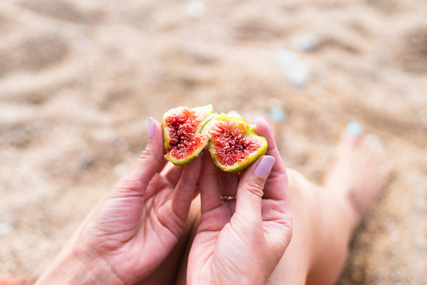 A young woman eats a ripe fig on the beach. Vacation and travel concept. Copy cpace. Selective focus. - Fotó, kép