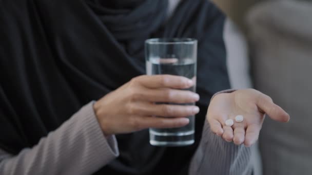 Close up unknown sick woman islamic muslim patient in hijab female hands holding pill from headache illness glass of mineral refreshing water prepare drink medicine drug tablet vitamin relief disease - Footage, Video