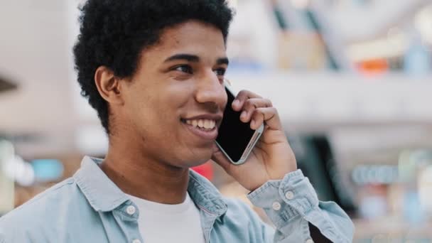 Afrikkalainen iloinen ystävällinen Afrikkalainen mies älypuhelin sisätiloissa puhuminen rento jutteleminen ystävien kanssa hymyilevä vastaus puhelu. Biracial kaveri on mukava puhua matkapuhelimen kauko neuvottelut - Materiaali, video