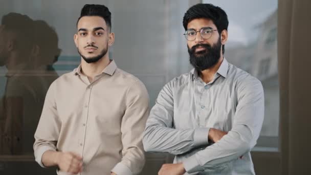 Two happy male colleagues multiracial diverse businesspeople partners men hispanic man arabian bearded guy smiling posing in office with crossed arms looking at camera confident corporate partnership - Imágenes, Vídeo
