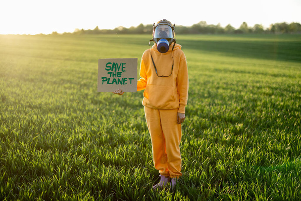 Pessoa em máscara de gás detém papelão com uma chamada para salvar o planeta - Foto, Imagem
